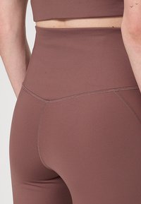 Közelkép egy személyről, aki magasan derékig érő, mauve színű, varrás nélküli leggings-t és egy hozzáillő, cropped felsőt visel, a hát és a derék részleteit bemutatva.