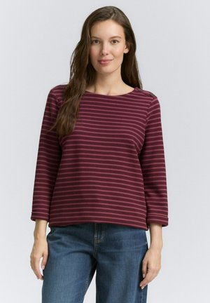T-shirt rayé bordeaux et rose à manches longues avec un col rond et des accents de boutons sur l'épaule, associé à un pantalon en denim bleu.