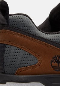 Primo piano di una sneaker in pelle marrone e mesh grigio vista laterale con logo nero e linguetta nera vicino al tallone.