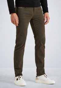Kaki slim-fit hlače s teksturiranim završetkom i pet džepova, uparene s bijelim niskim tenisicama s crnim i smeškastim detaljima.