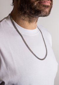 Collana in argento con anelli intrecciati, indossata su una semplice maglietta bianca. Aspetto testurizzato con una finitura lucida.