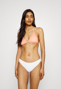 Top de biquíni cor de coral com bordas em scallop e alças ajustáveis, emparelhado com partes de baixo brancas de corte alto texturizadas. Tecido liso e elástico.