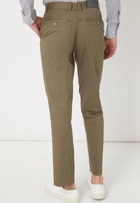Pantalones caqui de corte ajustado, con bolsillos traseros con botones decorativos y una textura suave. Combinados con zapatillas blancas.