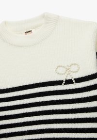 Gebreide trui met witte en zwarte horizontale strepen, geribbelde halslijn en een strikdetail met parelaccenten op de borst.