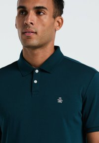 Polo bleu marine en tissu doux et texturé, avec une patte de boutonnage à trois boutons et un petit logo de pingouin brodé sur la poitrine.