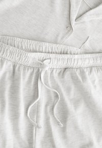 Pantalon de pyjama gris clair en tissu doux avec taille élastique et cordon, associé à un haut boutonné assorti, posé à plat.