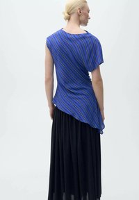 Top asimmetrico blu e nero con strisce diagonali, maniche corte e tessuto morbido, abbinato a una gonna nera fluida.
