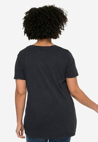 Camiseta negra de manga corta con un corte relajado, que presenta un escote redondo y una textura suave, vista desde la parte de atrás.
