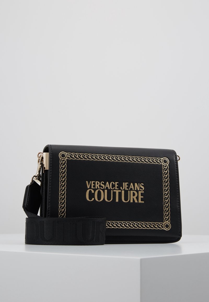 Borsa a tracolla rettangolare nera di Versace Jeans Couture con bordi in catena dorata e logo, dotata di una tracolla in tessuto larga e removibile.