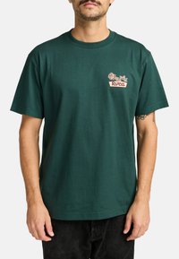 Camiseta de algodón verde oscuro con cuello redondo, que presenta un diseño en el pecho con una rosa y texto en colores contrastantes. Mangas cortas.