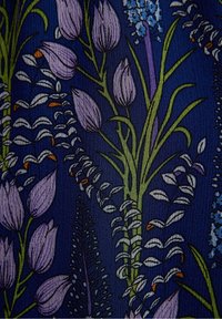 Mörkblått tyg med ett detaljerat blommönster som har lila tulpliknande knoppar, gröna stjälkar och små vita och orange-färgade blad.