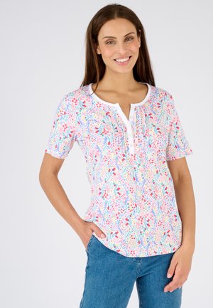 Blusa de manga corta con estampado floral en blanco, que presenta un colorido patrón de flores rojas, azules y verdes, con una tapeta de botones y un corte relajado.