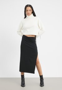 Kurzes weißes Rollkragensweatshirt mit geripptem Saum, kombiniert mit einem schwarzen, figurbetonten Maxirock mit seitlichem Schlitz und gerafftem Taillendetail.
