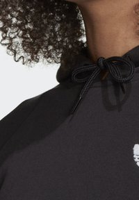 Svart hoodie med dragsko, med en texturerad yta och en vit broderad logotyp. Närbild på nackområdet och huvan.