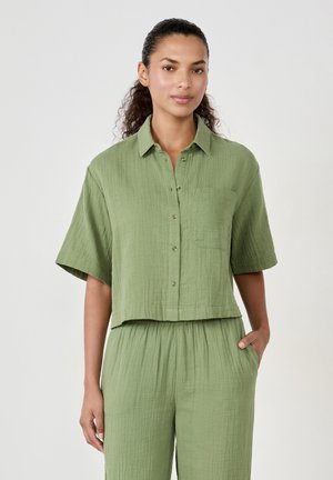 Relaxed-fit, short-sleeve shirt in textured olive green fabric, featuring a button-down front and a chest pocket. Cropped design.