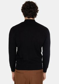 Maglione nero lavorato a maglia con maniche lunghe e collo alto. La parte posteriore presenta un design aderente, abbinato a pantaloni beige sartoriali.