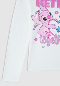 Biała koszula z długim rękawem z różowym, bajkowym kosmitą trzymającym serce oraz napisem "Lepiej razem" ozdobionym brokatem i różowymi ustami.