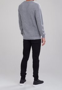 Grå stickad tröja med ett strukturerat mönster, tillsammans med svarta slim fit-byxor och grå skor med vita sulor.