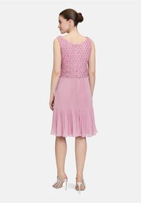 Różowa, plisowana sukienka z teksturowanym koralikowym gorsetem, bez rękawów i falbaniastym dołem. Połączona ze srebrnymi, strappy szpilkami.