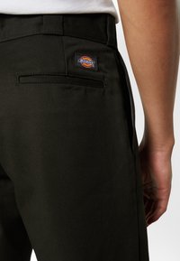 Svarta bomullsbukser med en bakficka med ett sydd Dickies-logotyp. Tyget har en slät yta och en välsydd passform.