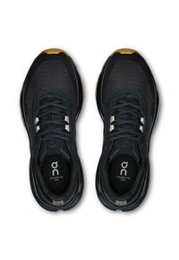 Chaussures de sport noires et grises avec une tige en mesh, présentant un design à motifs, des lacets et une semelle en caoutchouc. Accents en vert foncé et détail de logo.