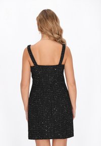 Schwarzes Kleid mit strukturiertem Muster, das breite Träger und ein tailliertes Oberteil hat. Das Material hat einen dezenten Schimmer mit silbernen Akzenten.