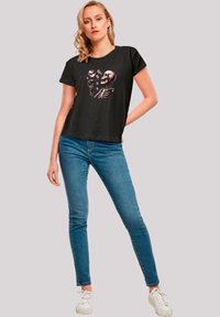 Black short-sleeve T-shirt featuring a skeleton graphic holding flowers. Paired with blue skinny jeans and white sneakers. Smooth texture.