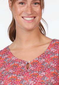 Bluse mit Blumenmuster in Rosa und Grau, runder Ausschnitt und einem kleinen Schlitzdetail. Mit einem kleinen Knopfverschluss am Hals.