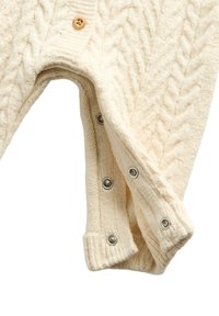 Krémový svetřík s copánkovým vzorem, který má knoflík na krku, patentky na manžetách a texturované vzory po celém materiálu.