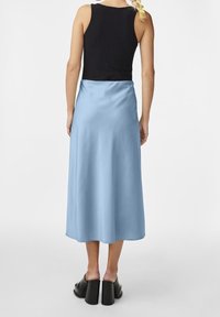 Satiininen vaaleansininen midihame, jossa on sileä pinta, yhdistetty mustaan hihattomaan toppiin. Malli käyttää lohkokorkoisia kenkiä.