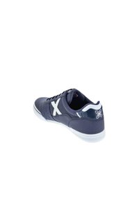 Zapatilla azul marino con acentos blancos, parte superior sintética lisa, puntera redondeada, diseño de cordones, paneles laterales texturizados y suela de goma blanca.