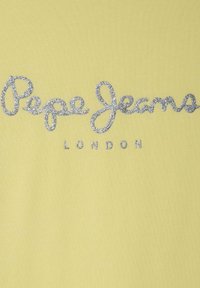 Geltona medvilninė marškinėlių su sidabrinėmis blizgančiomis "Pepe Jeans" užrašas, kuriame apačioje paprastu šriftu parašyta "LONDON". Sklandus paviršius, kasdieniškas dizainas.