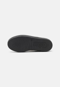 Black rubber sole with a wavy texture and prominent ridges. Features a raised logo with the brand name.