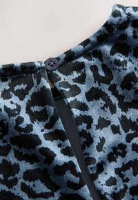 Melns un zils leoparda raksta audums ar gludu tekstūru, kakla izgriezumā kaklasaiša aizdarei izmantojot melnu pogu.