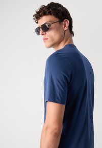Camiseta de algodón azul marino con mangas cortas, cuello redondo, textura suave y corte ajustado, combinada con gafas de sol oscuras.