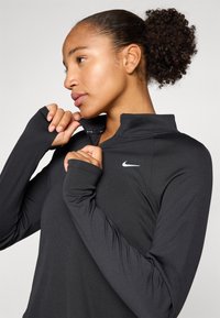Black long-sleeve athletic top with a quarter-zip collar, soft texture, and a small white logo on the chest, featuring thumbholes in cuffs.