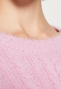 Suéter de punto texturizado en rosa con un acabado suave y esponjoso, que presenta un cuello acanalado y un patrón diagonal en toda la tela.