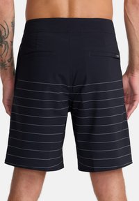 Shorts de bain noirs avec des rayures blanches horizontales, deux poches arrière et une texture de tissu lisse. Longueur mi-cuisse.