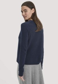 Marineblauer Wollpullover, runder Ausschnitt, lange Ärmel, taillierte Passform, strukturiertes Material, getragen mit einem hellgrauen Rock, sichtbare Nahtdetails.