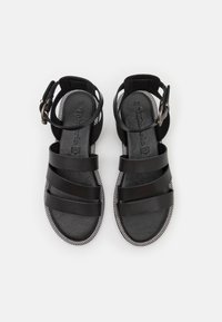 Sandales noires avec plusieurs brides sur le devant, en cuir, à semelle plate, et un accent tressé autour du bord. Sangle de cheville réglable incluse.