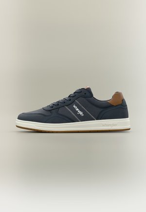 Navy blue low-top sneaker with white sole, brown heel accent, "Wrangler" branding on side and sole, lace-up design.