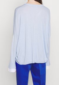 Ljusblå stickad tröja med lös passform, med ribbade ärmslut och rundad fåll, i kombination med blå byxor. Mjuk textur.