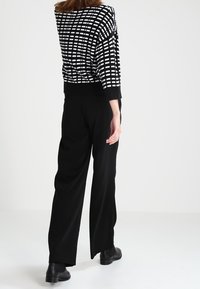 Czarnobiały sweter w kratę z opuszczonymi ramionami, zestawiony z eleganckimi czarnymi spodniami o szerokich nogawkach i stylowymi czarnymi botkami za kostkę.