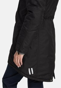 Czarny izolowany płaszcz z zamkiem błyskawicznym w bocznej kieszeni, elastycznym pasem, srebrnymi detalami oraz odblaskowymi paskami na krawędzi.