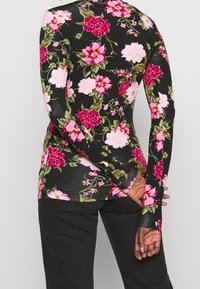 Långärmad topp i svart tyg med ett livligt rosa och rött blommönster. Fitted design med en rund halsringning och mjuk textur.
