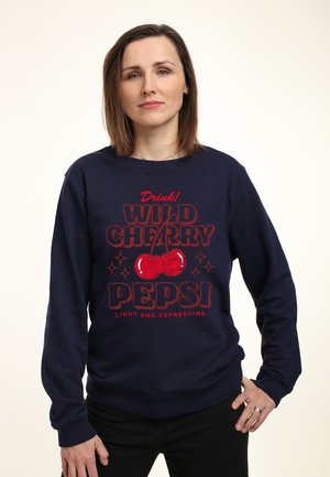 Sweatshirt marine avec "Drink! WILD CHERRY PEPSI" en lettres rouges, avec des graphismes de cerises et des accents d'étoiles. Manches et hem côtelés.