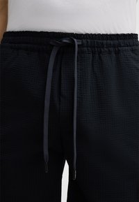 Zwarte getextureerde joggerbroeken met een elastische tailleband en verstelbare trekkoord. Heeft een gemusterde stof voor extra diepte.