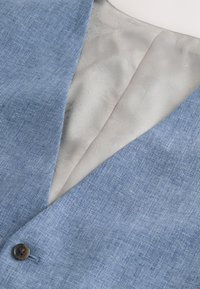 Gros plan d'un blazer bleu clair texturé avec un seul bouton marron et une doublure intérieure lisse gris clair visible.