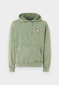 Sweat à capuche vert olive avec poche avant kangourou, capuche à cordon de serrage et un petit patch globe à l'intérieur d'un pentagone orange sur le côté gauche de la poitrine.