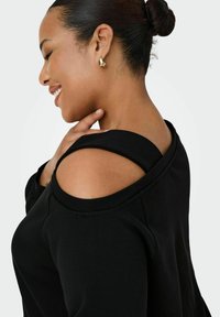 Čierna mikina s off-shoulder dizajnom, so soft touch textúrou a viditeľnými švami. Zlaté náušnice zvýrazňujú dekolt.